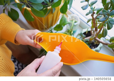 Top view of Hands holding a bottle of hydrogen peroxide over a yellow watering can 140505658
