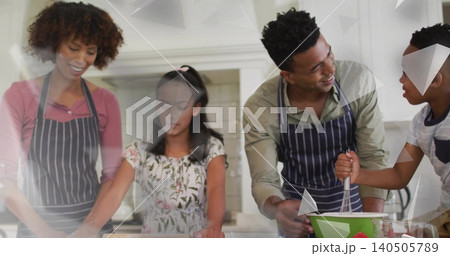 Gathering family of four rolling and whisking dough at home kitchen island, wearing striped aprons 140505789