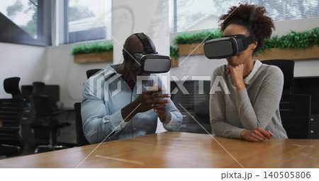 Gesturing man leaning forward, woman resting chin, wearing VR gear, office attire at long table Gesturing man leaning forward, woman resting chin, wearing VR gear, office attire at long table 140505806