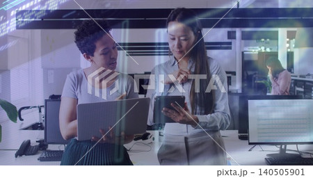 Reviewing two coworkers pointing at laptop and tapping tablet in tech hub in workwear with monitors Reviewing two coworkers pointing at laptop and tapping tablet in tech hub in workwear with monitors 140505901