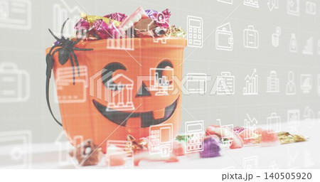 Displaying orange jackolantern bucket holding wrapped candies, spider on white table, finance icons Displaying orange jackolantern bucket holding wrapped candies, spider on white table, finance icons 140505920