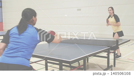 Playing two female players rallying at gym table, blue shirt, yellow skirt, red paddles, white ball Playing two female players rallying at gym table, blue shirt, yellow skirt, red paddles, white ball 140506108