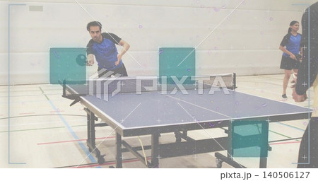 Playing left-side man wearing blue-black kit, hitting ball with paddle at table tennis table in gym Playing left-side man wearing blue-black kit, hitting ball with paddle at table tennis table in gym 140506127