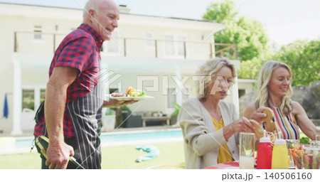 Serving senior man wearing red-black plaid shirt and striped apron holding plate and tongs poolside Serving senior man wearing red-black plaid shirt and striped apron holding plate and tongs poolside 140506160