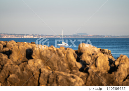 Sailboat journeying across calm blue waters near rocky coastline at sunset 140506485