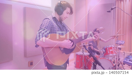 Playing guitarist in checked shirt, headphones, tracking acoustic guitar in studio, red drum kit Playing guitarist in checked shirt, headphones, tracking acoustic guitar in studio, red drum kit 140507154