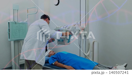 Positioning tech leaning over senior woman in blue gown on table in X-ray room adjusting detector 140507241