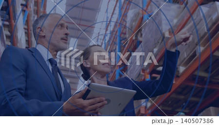 Inspecting two managers in suits reviewing stock in warehouse near pallet racking, holding tablet Inspecting two managers in suits reviewing stock in warehouse near pallet racking, holding tablet 140507386