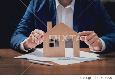 Man proposing signing a estate insurance policy, the agent is holding the wooden house model. Estate insurance concept. Man proposing signing a estate insurance policy, the agent is holding the wooden house model. Estate insurance concept. 140507990