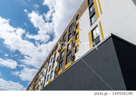 A modern building with yellow accents is seen under a blue sky filled with clouds. This structure is located in an urban setting A modern building with yellow accents is seen under a blue sky filled with clouds. This structure is located in an urban setting 140508196