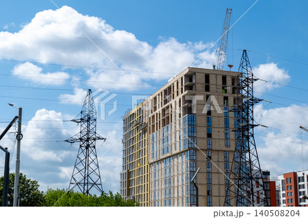 Workers are busy on a high rise building while power lines stand tall against the blue sky. Cranes are lifting materials for the project 140508204