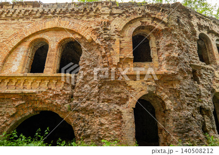 Crumbling walls of a brick building stand among trees. Openings show empty spaces inside. Nature surrounds the old structure 140508212