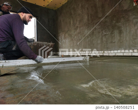 Construction worker carefully screeding wet concrete, leveling a new subfloor during building renovation, creating a smooth surface for future finishing work. Construction worker carefully screeding wet concrete, leveling a new subfloor during building renovation, creating a smooth surface for future finishing work. 140508251
