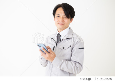 スマホを持つグレーの作業着のミドル男性ビジネスマン白バック 140508680