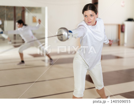 Woman in uniforms practice fencing techniques with foils in their hands. Woman in uniforms practice fencing techniques with foils in their hands. 140509055