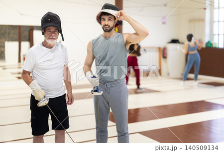 Portrait of an elderly coach with rapier in his hands and atletic man during fencing training in gym Portrait of an elderly coach with rapier in his hands and atletic man during fencing training in gym 140509134