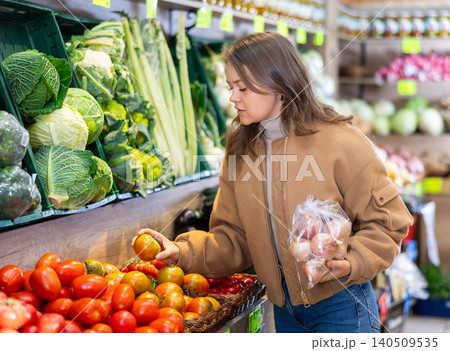 Young female shopper selects and buys tomatoes in supermarket 140509535
