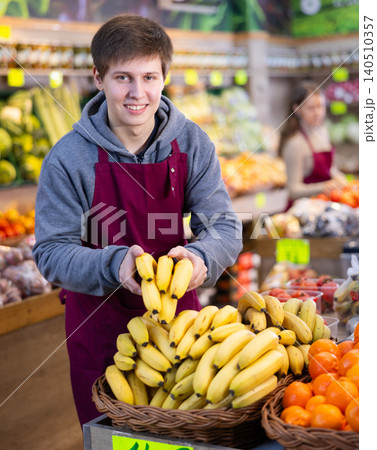 Young salesman placing bananas in a market basket in large grocery store Young salesman placing bananas in a market basket in large grocery store 140510357