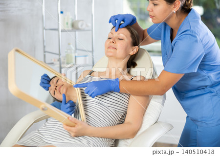 Woman cosmetologist examines patients forehead after lifting procedure and palpates forehead area Woman cosmetologist examines patients forehead after lifting procedure and palpates forehead area 140510418