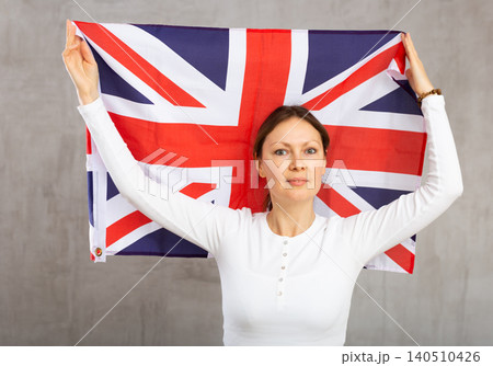 Happy young woman holding flag of Great Britain against unicoloured background Happy young woman holding flag of Great Britain against unicoloured background 140510426