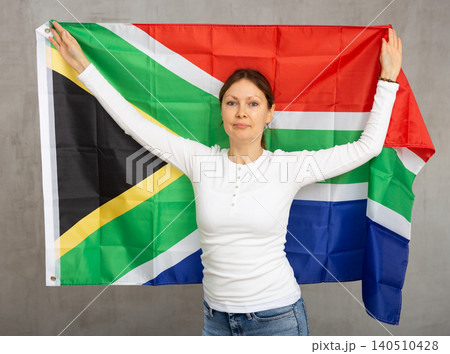 Confident middle-aged woman waving national flag of South Africa while looking at camera at gray wall background Confident middle-aged woman waving national flag of South Africa while looking at camera at gray wall background 140510428