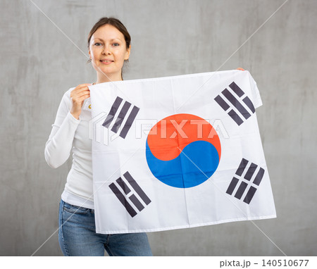 Smiling relaxed woman waving national flag of South Korea while looking at camera at gray wall background Smiling relaxed woman waving national flag of South Korea while looking at camera at gray wall background 140510677