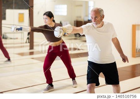 Elderly man practicing fencing movements in gym 140510756