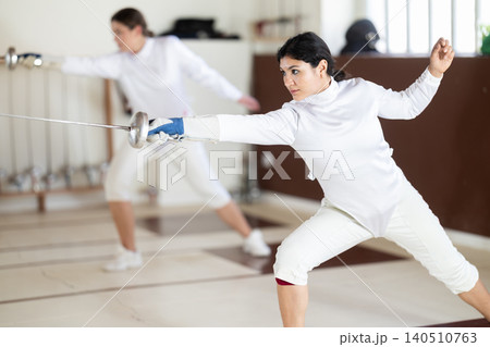 Men and women in white uniforms practice fencing techniques with foils in hands Men and women in white uniforms practice fencing techniques with foils in hands 140510763
