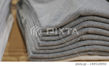 Close-up of neatly folded grey t-shirts stacked on a wooden shelf Close-up of neatly folded grey t-shirts stacked on a wooden shelf 140510950