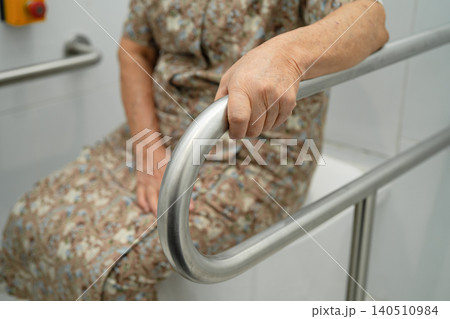 Asian elderly woman patient use toilet support rail in bathroom. Asian elderly woman patient use toilet support rail in bathroom. 140510984