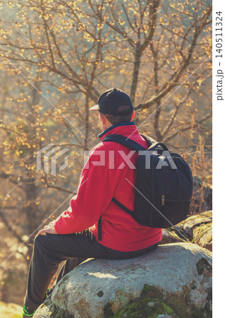 A tourist sits on a rock above a beautiful canyon on a sunny autumn day. The man looks at the river A tourist sits on a rock above a beautiful canyon on a sunny autumn day. The man looks at the river 140511324
