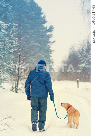 Man and dog are best friends. A man with a dog walks along the road along the forest in a snowy winter 140511448