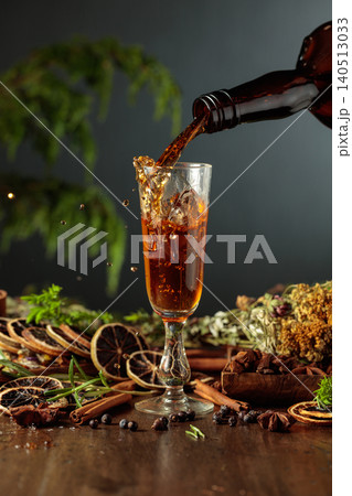 Herbal bitter liqueur is poured from a dark glass vintage bottle into a glass. Herbal bitter liqueur is poured from a dark glass vintage bottle into a glass. 140513033