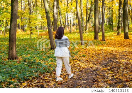 Woman walking through vibrant autumn forest. Girl relaxing in fall park with golden maple leaf on ground. Seasonal nature exploration, leisure activity and peaceful outdoor lifestyle concept. 140513138