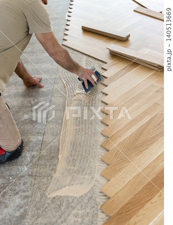 Worker applying parquet flooring adhesive with notched trowel during home construction, top view Worker applying parquet flooring adhesive with notched trowel during home construction, top view 140513669