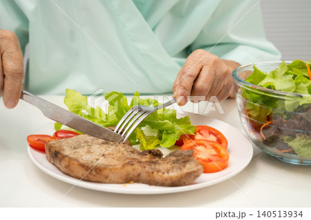 Asian elderly woman patient eating pork chop stake and vegetable salad for healthy food in hospital. Asian elderly woman patient eating pork chop stake and vegetable salad for healthy food in hospital. 140513934
