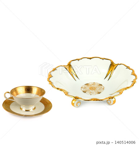 Elegant vintage porcelain teacup with saucer and matching large footed fruit bowl decorated with luxury gold patterns, isolated on a clean white background, horizontal frame orientation. 140514006