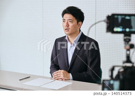 収録のスタジオで撮影の為にビデオカメラに向かって話すスーツ姿の30代の日本人の男性のアナウンサー 140514373