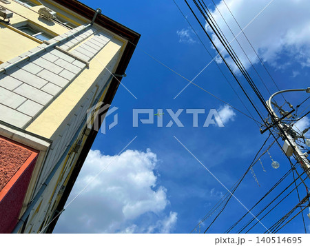 Low angle upward view of airplane in the sky between urban building corner and power lines Low angle upward view of airplane in the sky between urban building corner and power lines 140514695