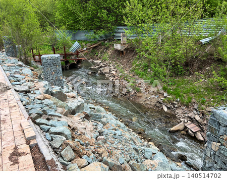 Rocky riverbank with rubble and construction debris along narrow stream channel in urban area Rocky riverbank with rubble and construction debris along narrow stream channel in urban area 140514702