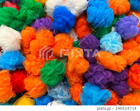 Colorful assortment of multicolored mesh bath sponge poufs piled together in a market 140514714