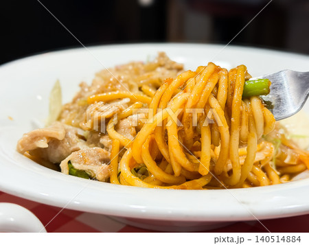 ナポリタンと豚肉の生姜焼きが乗ったお皿。ナポリタンを箸で持ち上げている様子。 140514884