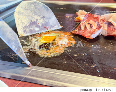 鉄板料理のイカ焼き。鉄板で焼いた新鮮なイカの横で、イカの肝とバターと醤油を混ぜているところ。 鉄板料理のイカ焼き。鉄板で焼いた新鮮なイカの横で、イカの肝とバターと醤油を混ぜているところ。 140514891