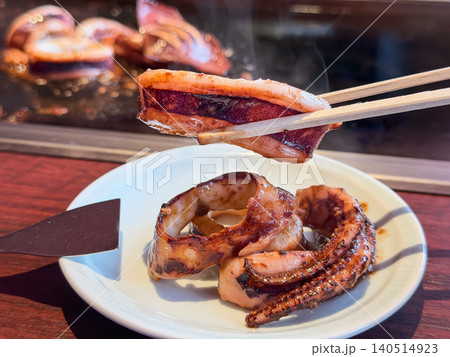 鉄板料理のイカ焼き。鉄板で焼いた美味しいイカを箸で持ち上げている様子。 鉄板料理のイカ焼き。鉄板で焼いた美味しいイカを箸で持ち上げている様子。 140514923
