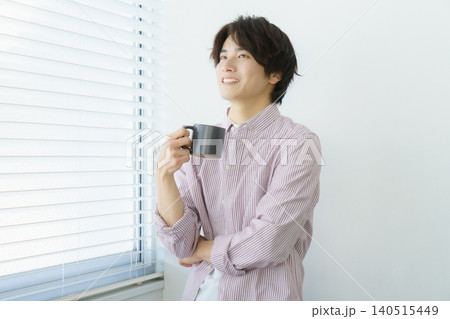 窓際に立つ縦縞のシャツを着てマグカップを持つ若い日本人男性のポートレート 窓際に立つ縦縞のシャツを着てマグカップを持つ若い日本人男性のポートレート 140515449