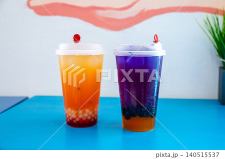 Fruit bubble tea and blue galaxy bubble tea with butterfly pea tea and boba pearl. Refreshing cold summer drinks in plastic cups. Popular Asian street food beverage on blue table. Fruit bubble tea and blue galaxy bubble tea with butterfly pea tea and boba pearl. Refreshing cold summer drinks in plastic cups. Popular Asian street food beverage on blue table. 140515537