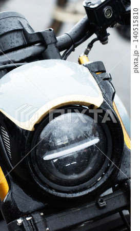 Motorcycle front headlight and handlebars detail on wet surface with raindrops, close-up view of vehicle part, engineering and design concept, vertical photo Motorcycle front headlight and handlebars detail on wet surface with raindrops, close-up view of vehicle part, engineering and design concept, vertical photo 140515810
