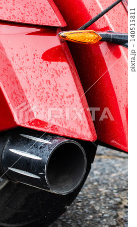 Vibrant red motorcycle rear fender displaying many clear water droplets, contrasting black exhaust pipe with subtle silver stripes, prominent amber turn signal, capturing wet vehicle conditions after Vibrant red motorcycle rear fender displaying many clear water droplets, contrasting black exhaust pipe with subtle silver stripes, prominent amber turn signal, capturing wet vehicle conditions after 140515811