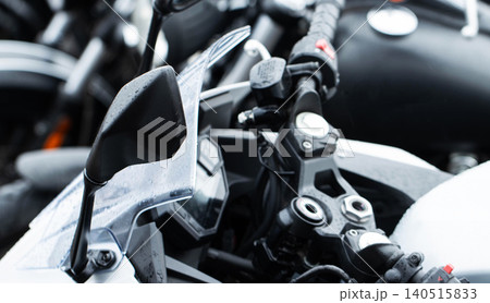 Close-up view of modern motorcycle handlebar, rearview mirror, and wet windshield, showing details of controls and sleek design of vehicle after rain or washing. Close-up view of modern motorcycle handlebar, rearview mirror, and wet windshield, showing details of controls and sleek design of vehicle after rain or washing. 140515833