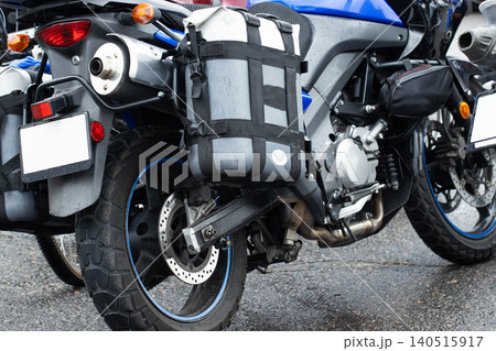 Adventure touring motorcycle parked on wet asphalt road surface. Close up view of rear wheel, exhaust pipe, taillight, and luggage bags for long distance travel. Adventure touring motorcycle parked on wet asphalt road surface. Close up view of rear wheel, exhaust pipe, taillight, and luggage bags for long distance travel. 140515917